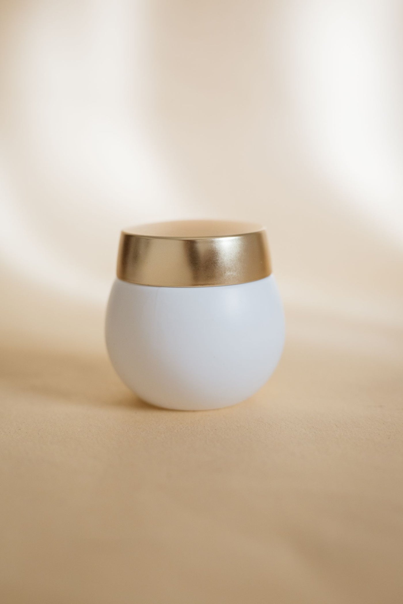 Pot de crème blanc au couvercle doré sur fond crème