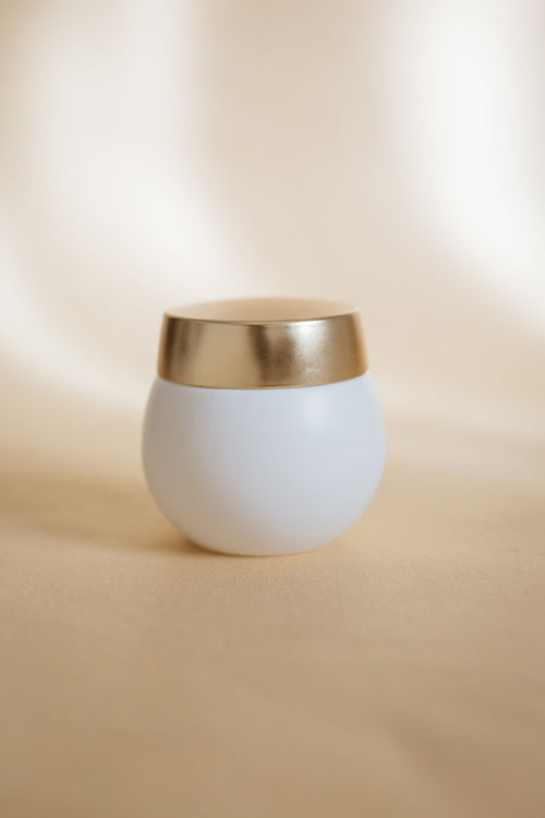 Pot de crème blanc au couvercle doré sur fond crème